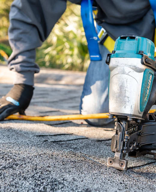 Roofer installing asphalt shingles with a pneumatic nailer
